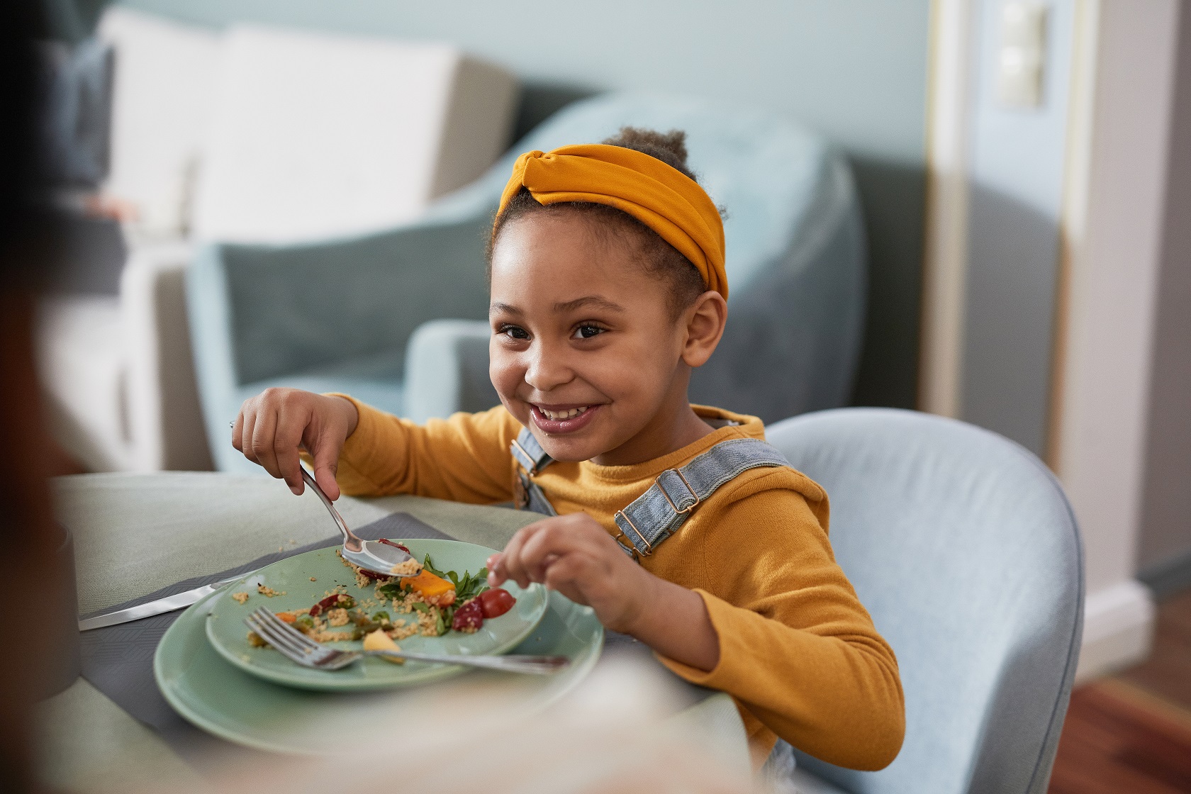 A smiling child eats a meal at a table.