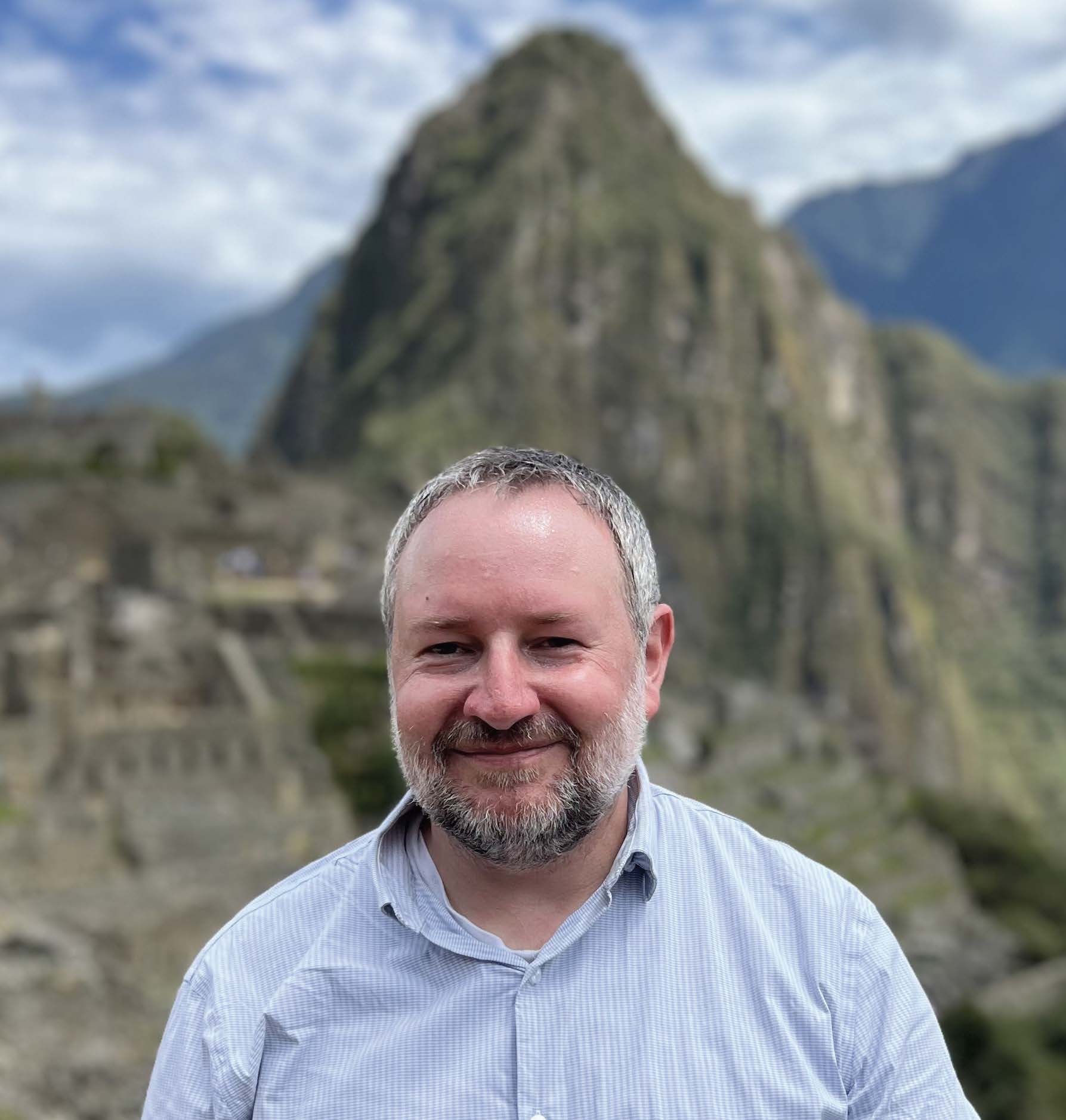 Evan Cale, Ph.D. photographed outside with a large rock and a mountain in the background