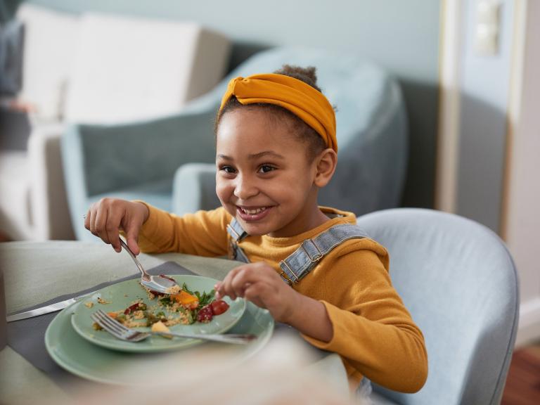 A smiling child eats a meal at a table.