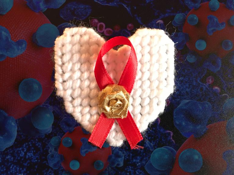 HIV ribbon on a heart shaped pin in front of virus and cells