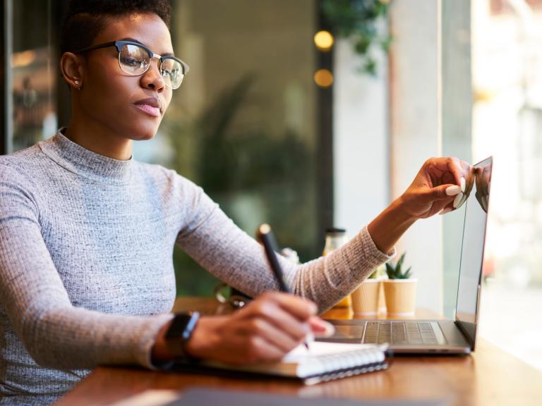 Serious black lady with glasses writing down plans in notepad.