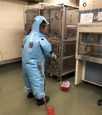 A man in a blue personal protective equipment suit with a red airline attached to his right hip practices opening a cage.