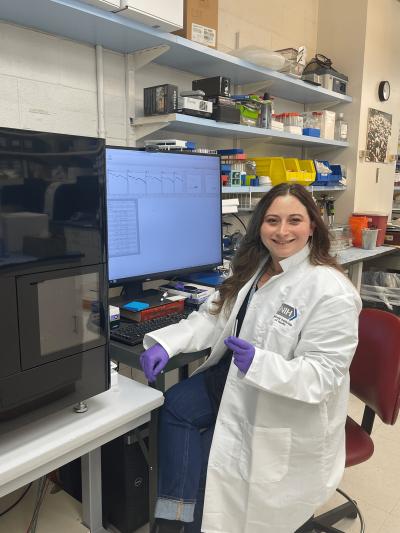 Woman in lab coat sits at a computer in a lab.