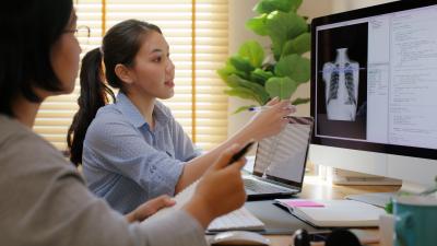 Two women look at a computer screen with coded data and an X-ray