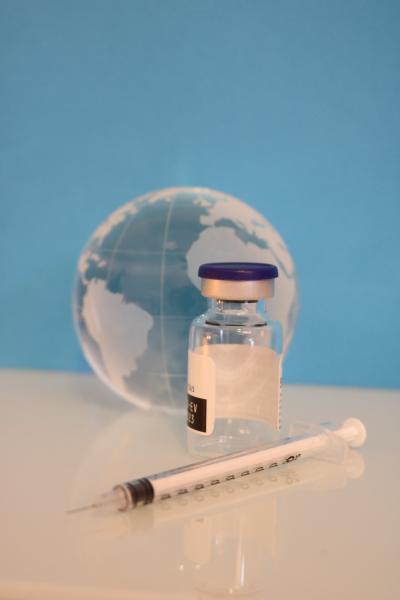 an empty vaccine vial and syringe sit in front of a glass globe