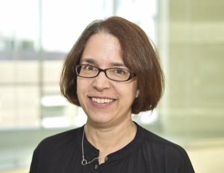 A professional headshot of Dr. Cuomo, standing in a bright atrium. She has short brown hair and is wearing glasses.