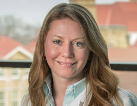 A professional headshot of Dr. Nett standing in front of a window. She has long blonde hair, and is wearing a lab coat.