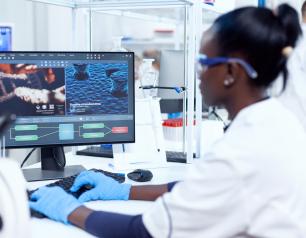 A researcher in a laboratory looks at a computer screen displaying DNA data.