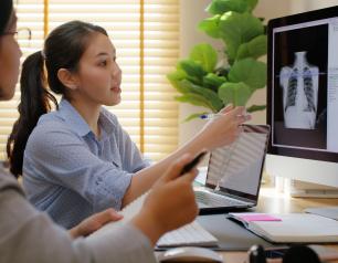 Two women look at a computer screen with coded data and an X-ray