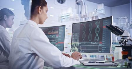 Scientists at computers with data and images on the screen and a microscope next to it.
